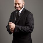 Portrait-Personal Branding photo of a male in a black suit with a black tie adjusting his cuffs while smiling.