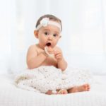 Portrait of a surprised baby wearing a white flower headband and playing with white pearl beads.