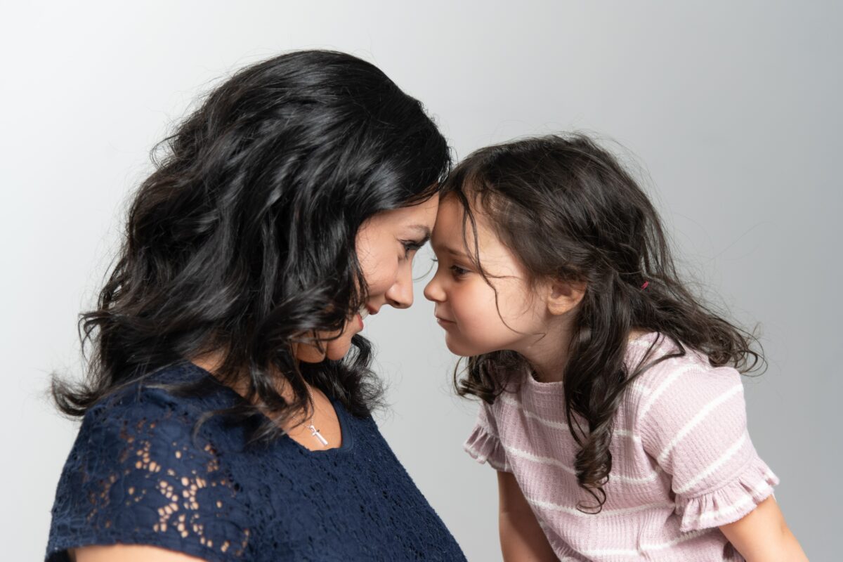 mother and her young daughter stare each other down in a playful way while touching their foreheads