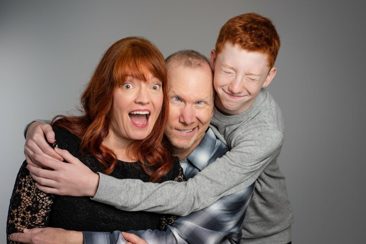 Mother, Father, and son do a group hug while making silly faces towards the camera