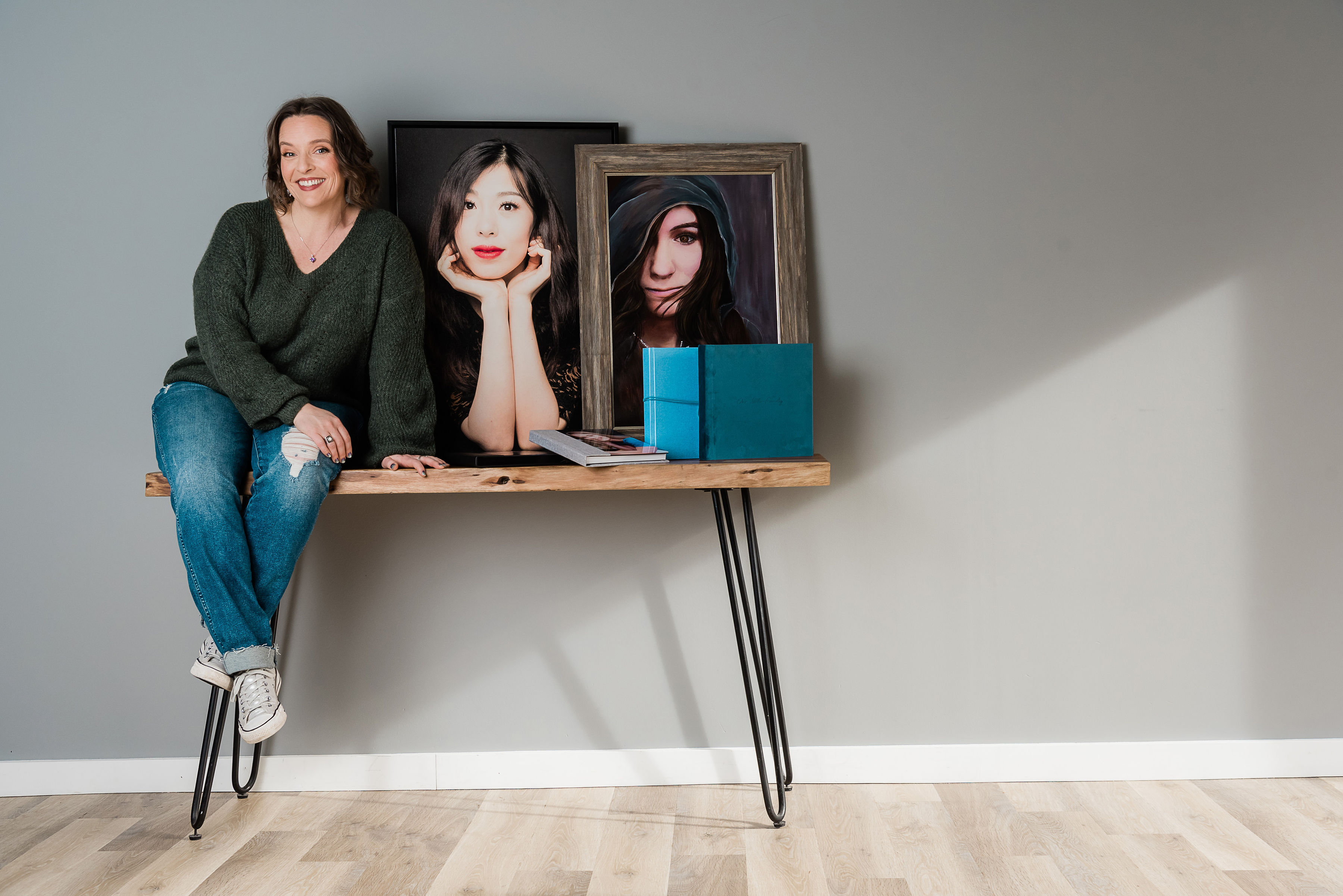 Photo of a woman sitting on a table next to framed portraits and photo albums.