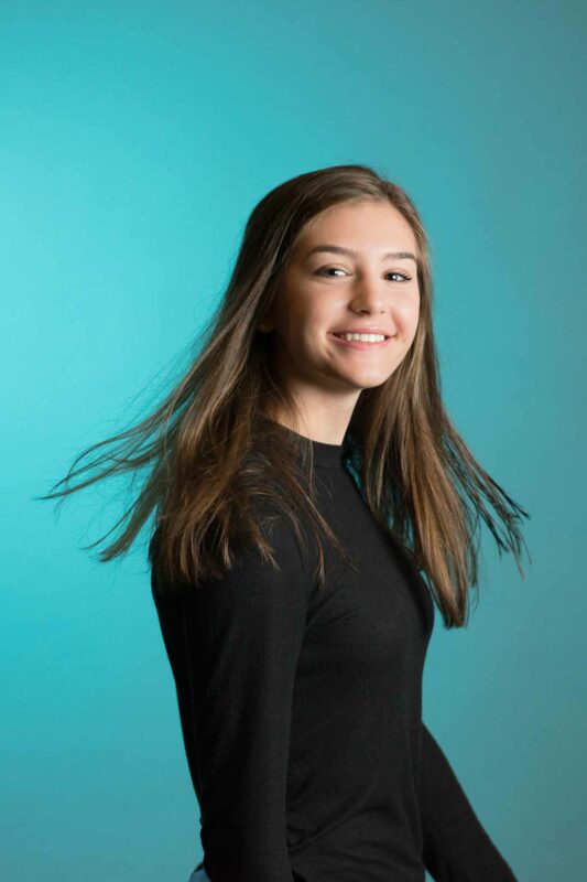 Young lady posing for portrait by twirling her head. Long hair smiling with backdrop.