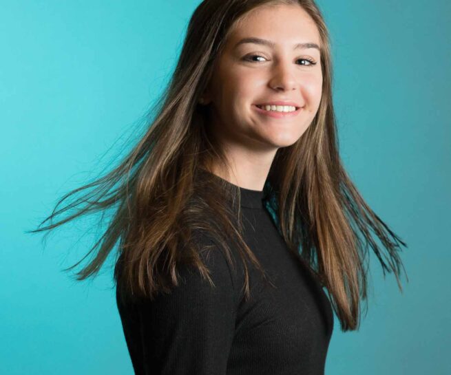 Young lady posing for portrait by twirling her head. Long hair smiling with backdrop.