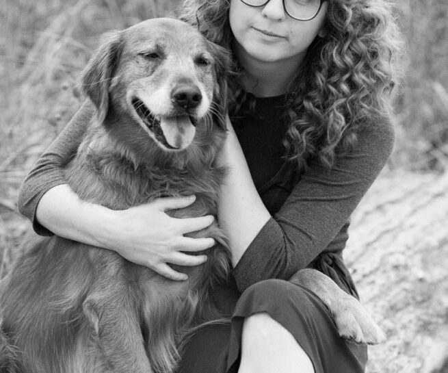 black and white photo of a dog and a teenage girl with curly hair past shoulders, wearing glasses.
