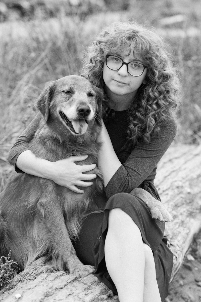 black and white photo of a dog and a teenage girl with curly hair past shoulders, wearing glasses.