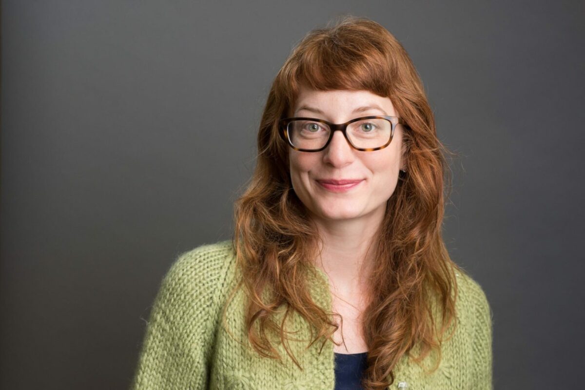 Woman with long red hair wearing glasses, posing for photo.