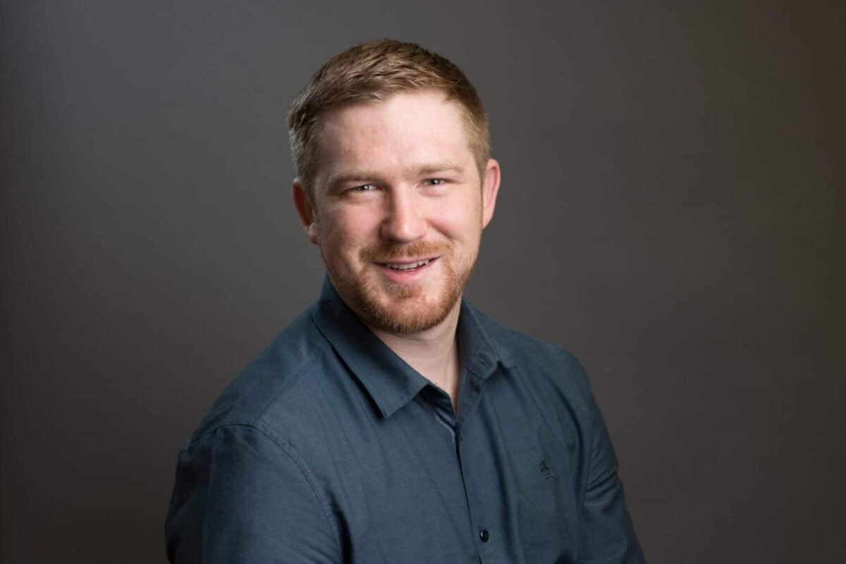 Man posing for photo wearing a dark long sleeve open collar shirt.