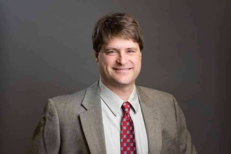 Man wearing a suit and tie posing for a headshot photo.