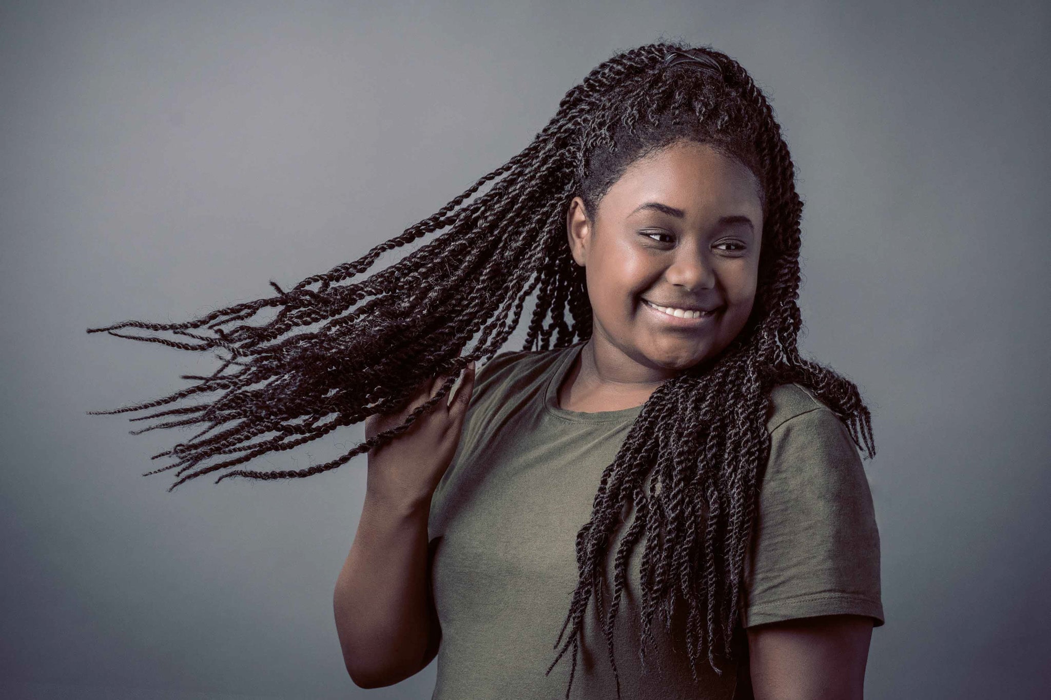 Girl smiling and swinging her long, braided black hair around during a photo shoot.