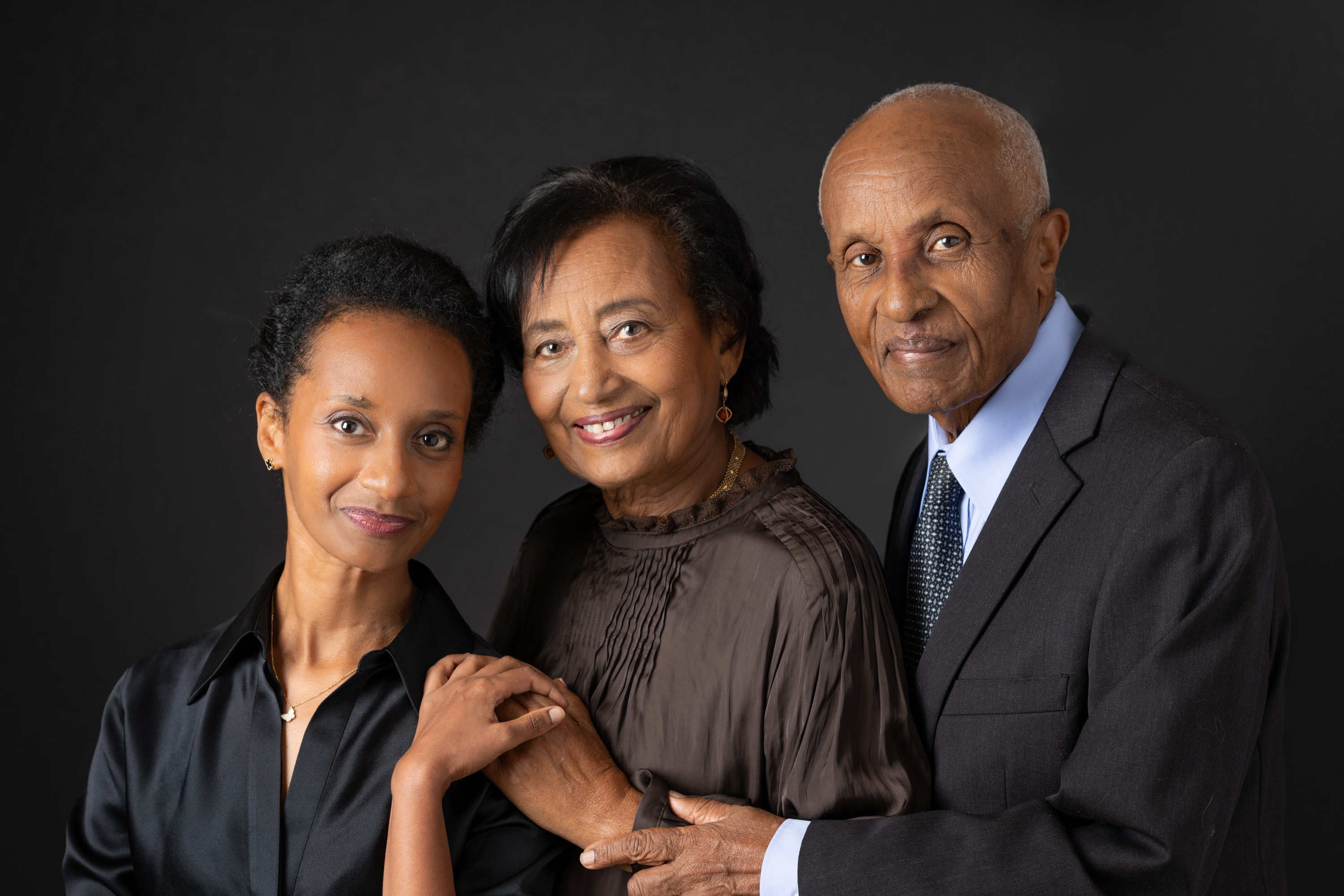 Family of three dressed up in front of a black background